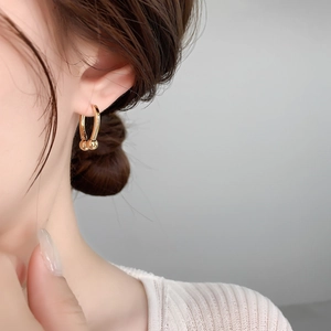 Close-up of a gold U-shaped link earring with polished metal spheres on a model