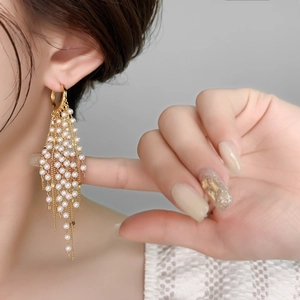 Gros plan sur de longues boucles d'oreilles dorées à pampilles et perles multicouches