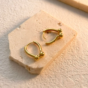 Detail of golden U-shaped huggie earrings with metal ball charms on stone texture