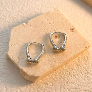 Polished silver horseshoe earrings with double bead details on a textured stone base