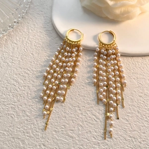 Détail de longues boucles d'oreilles dorées à pampilles et perles blanches sur fond blanc