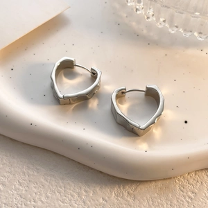 Detailed view of polished irregular heart-shaped silver hoop earrings on a textured tray