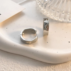 Detailed close-up of irregular silver geometric huggie earrings on a white ceramic tray