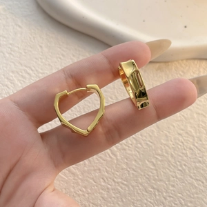 Detail of hand-held gold heart hoop earrings with irregular hammered liquid metal texture