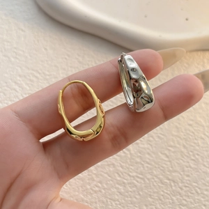Detailed close-up of irregular mirror-finish hoop earrings in gold and silver metal