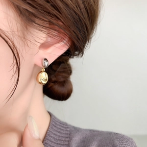 Close-up of minimalist gold and silver contrast bean earrings worn on a model ear