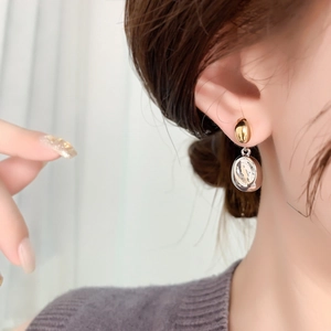 Detail of minimalist mixed-metal drop earrings with gold stud and silver oval hoop