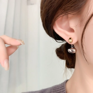 Close-up of 18K gold bean earrings worn on ear showing polished mirror finish effect