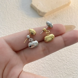 Macro view of minimalist mixed-tone gold and silver bean stud earrings held by hand