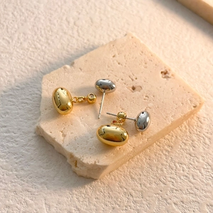 Macro shot of asymmetric gold and silver bean stud earrings on a textured stone surface