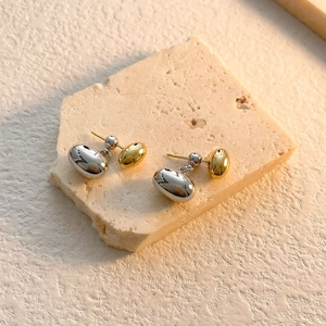 Close-up of minimalist two-tone gold and silver bean drop earrings on stone base