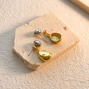 Detail view of bicolor gold and silver bean-shaped drop earrings on stone base
