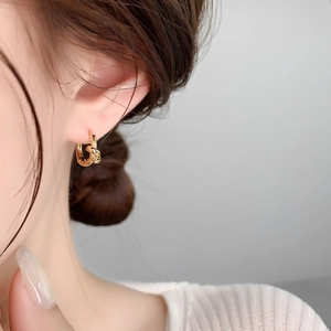 Close-up of a minimalist gold-plated knot hoop earring worn by a model in soft light