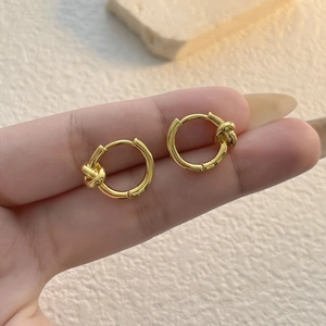 Minimalist gold knot hoop earrings held in hand against a warm textured background
