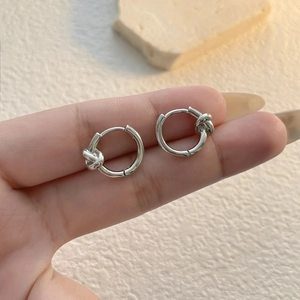 Close-up of hand holding silver geometric knot hoop earrings for size reference