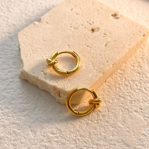 Detailed view of gold knotted hoop earrings on a textured stone display pedestal