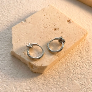Detailed view of silver knot hoop earrings on a textured stone display pedestal