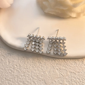 Macro shot of silver zircon tassel earrings with four strands on white ceramic base