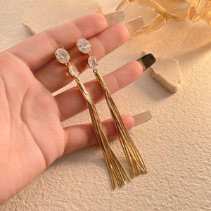 Elegant gold tassel earrings with oval cubic zirconia stones held by hand