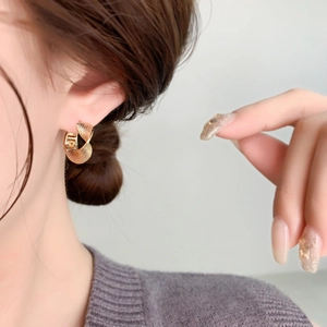 Detailed close-up of golden twisted hoop earrings with fine grain texture on earlobe