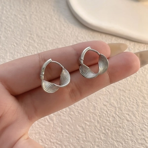 Macro shot of silver twisted hoop earrings with polished and frosted metal texture