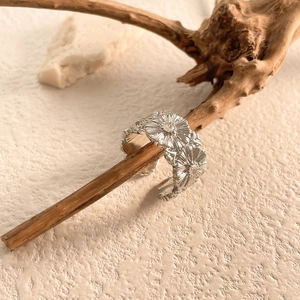 Dettaglio dell'anello a margherita in argento con zircone su un ramo di legno