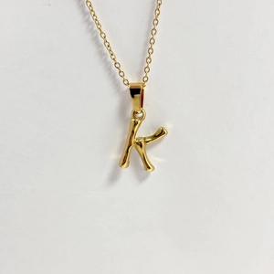 Collier doré avec pendentif lettre K au design bambou sur fond blanc épuré