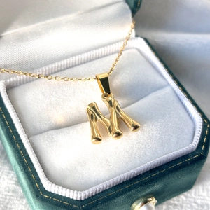 Vue macro du pendentif lettre M doré avec texture bambou dans un écrin de bijoux en velours
