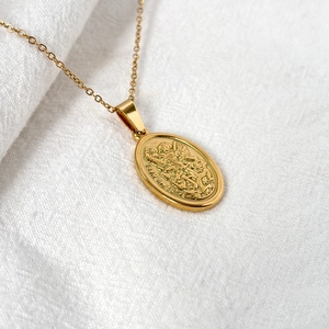 Detailed view of Saint Michael embossed gold oval pendant necklace on white fabric