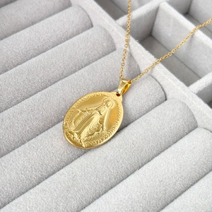 Macro detail of gold oval Virgin Mary pendant necklace with French religious engraving