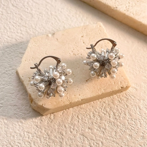 Macro detail of silver snowflake pearl earrings with zircons on a textured stone