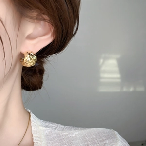 Macro detail of gold C-shaped earrings featuring a vintage woven texture and elegant metallic finish