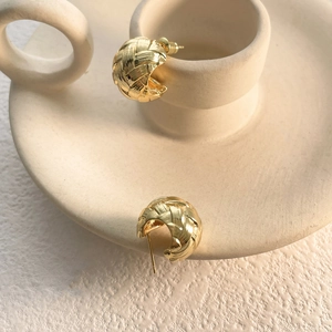 Close-up of golden hoop earrings featuring intricate woven texture and hollow design