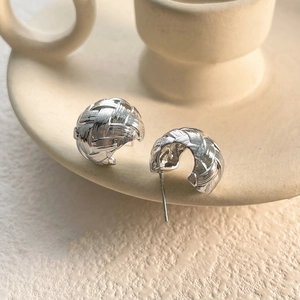 Macro shot of silver woven texture stud earrings on a beige ceramic dish edge