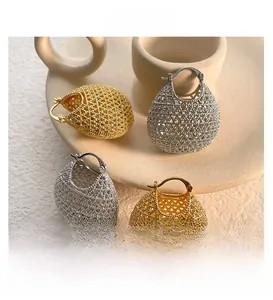 Detailed close-up of hollow gold and silver basket-style earrings on ceramic tray