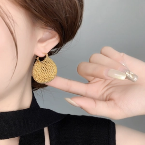 Macro detail of vintage gold lucky bag hoop earring with hollow woven texture on model