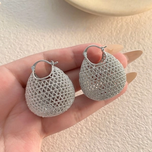 Detailed view of silver hollow woven water-drop earrings held by a hand
