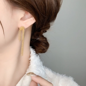Detailed view of long tiered bead tassel earrings in gold plating on a female model