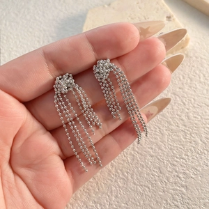 Detailed view of silver-tone ball chain tassel earrings held against a textured stone backdrop