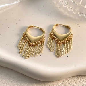 Détail des boucles d'oreilles à pampilles dorées sur un plateau en céramique