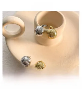 Detailed close-up of spherical gold and silver mesh textured earrings in a ceramic bowl
