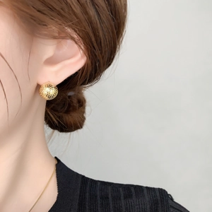 Detail of 18k gold plated ball stud earrings with mesh texture on model's ear