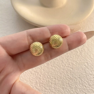 Textured gold-plated ball stud earrings with snake scale pattern held in hand