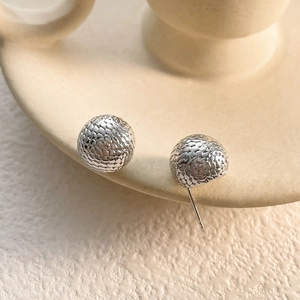 Macro shot of silver sphere earrings featuring unique textured scale patterns on the surface