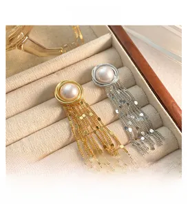 Detail of long tassel earrings with faux pearl studs and shiny gold and silver chains