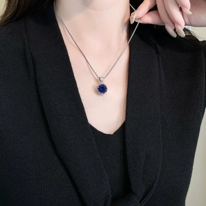 Close-up of a silver box chain necklace featuring a dark blue zircon bud pendant