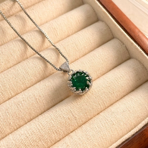 Macro detail of round green zircon pendant on box chain inside a velvet jewelry box