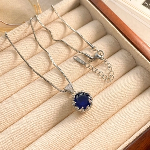Close-up of a sapphire blue stone pendant on a silver box chain in a gift box