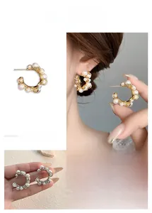Detail of C-shaped hoop earrings featuring white pearls in gold and silver finish