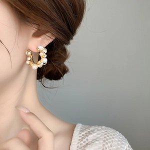 Detail of C-shaped hoop earring featuring white pearls wrapped in gold wire on a model